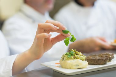 Female chef garnishing a plate with steak clipart