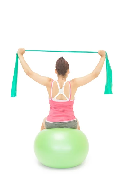Sporty brunette stretching with resistance band sitting on exercise ball — Stock Photo, Image
