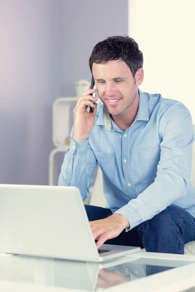 Sorridente uomo casuale utilizzando laptop e telefono — Foto Stock