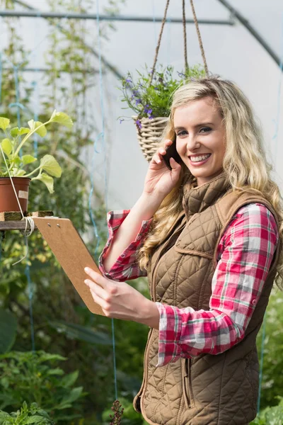 Phoning woman holding a clipboard in her green house — Stock Photo, Image