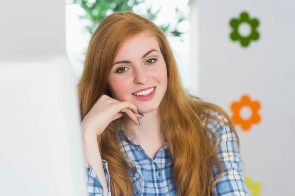 Atractiva pelirroja sentada en su escritorio sonriendo a la cámara — Foto de Stock