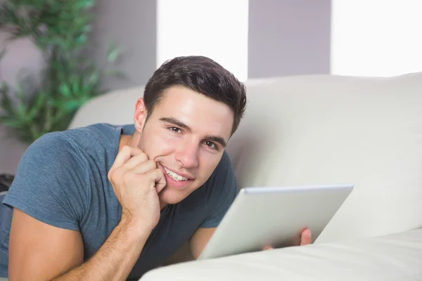 Lächelnder schöner Mann liegt mit Tablet auf Couch — Stockfoto