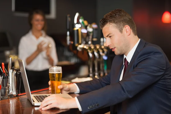 在他的笔记本电脑上工作时喝啤酒的商人 — 图库照片