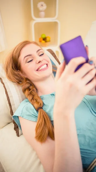 Sonriente pelirroja acostada en el sofá enviando un mensaje de texto —  Fotos de Stock