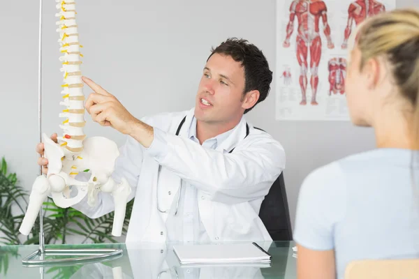 Handsome doctor showing a patient something on skeleton model — Stock Photo, Image