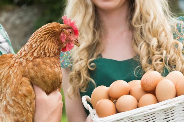 Pareja joven sosteniendo pollo y cesta de huevos — Foto de Stock