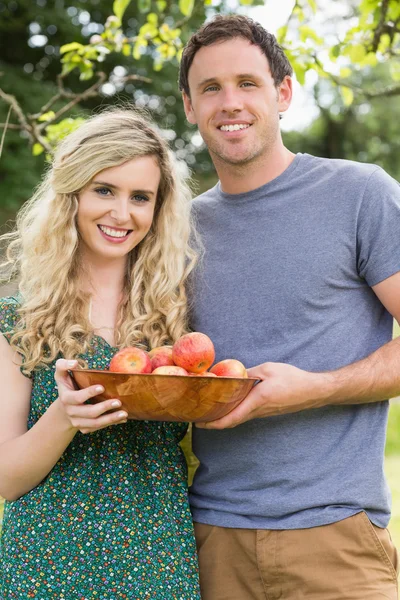 Pareja joven sosteniendo un tazón con manzanas — Foto de Stock