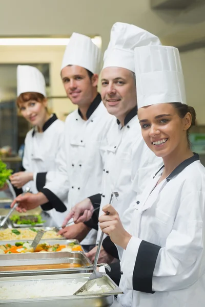 Quatro chefs trabalhando em bandejas de serviço sorrindo para a câmera — Fotografia de Stock