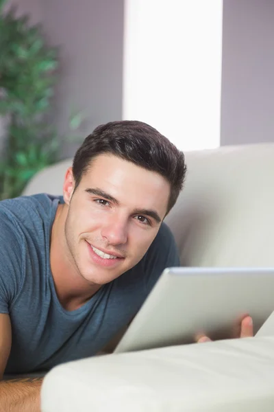 Zufriedener schöner Mann liegt mit Tablet auf Couch — Stockfoto