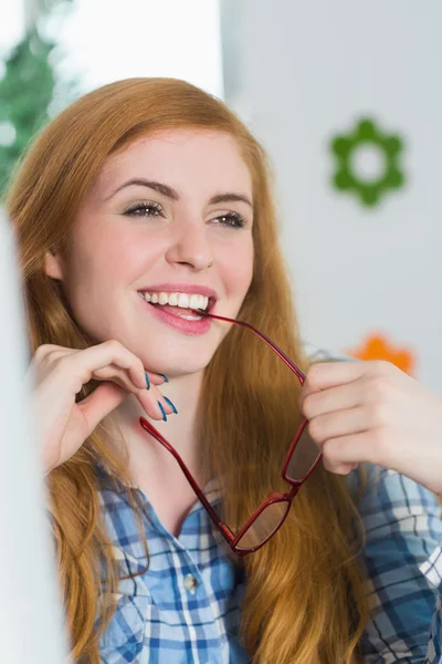 Belle rousse assise à son bureau et mordant ses lunettes — Photo