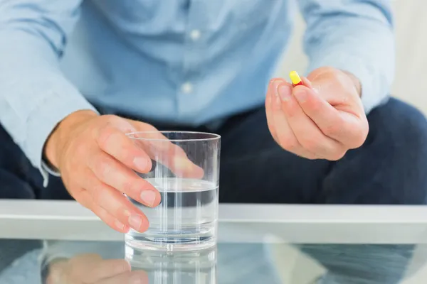 Close up of man holding glass of water and pill — Stock Photo, Image