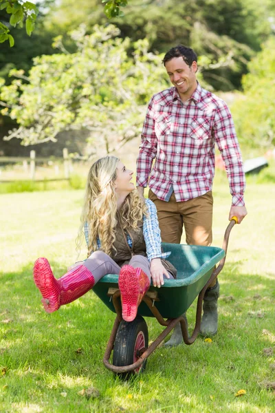 Happy man pushing his girlfriend in a wheelbarrow — Stock Photo, Image