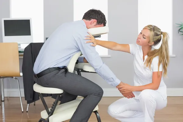 Masseuse treating clients arm in massage chair — Stock Photo, Image