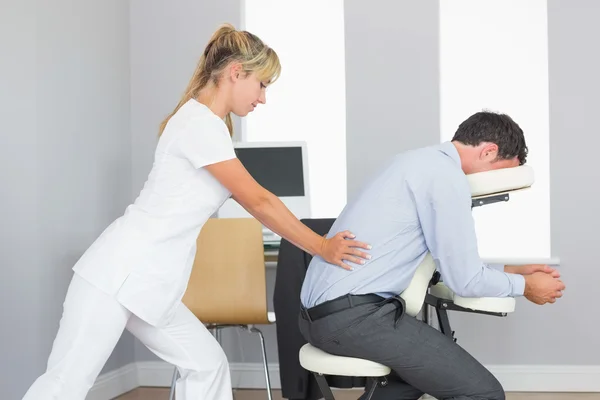 Массажист лечит клиентов ниже спины в массажном кресле — стоковое фото