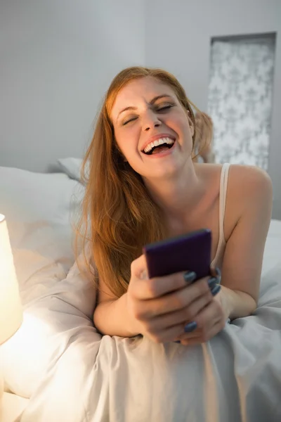 Směje se zrzka ležící na posteli odeslání textové — Stock fotografie