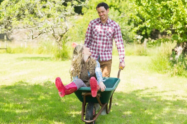 Happy man pushing his laughing girlfriend in a wheelbarrow — Stock Photo, Image