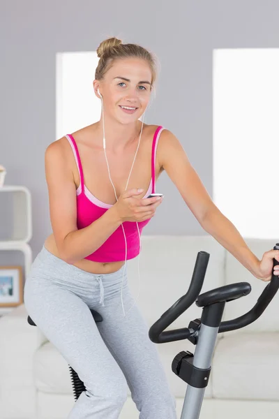 Sporty smiling blonde training on exercise bike listening to music — Stock Photo, Image