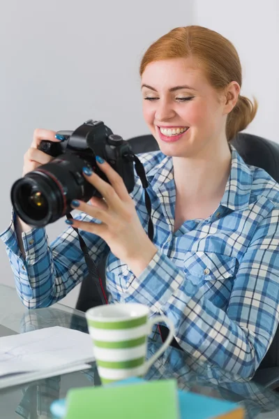 Glückliche Fotografin sitzt an ihrem Schreibtisch und blickt in die Kamera — Stockfoto