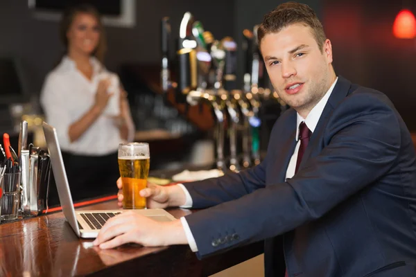 Geschäftsmann trinkt ein Pint während er an seinem Laptop arbeitet — Stockfoto