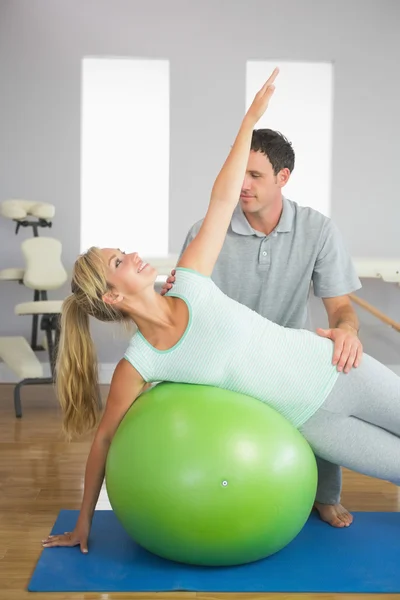 Fisioterapeuta sonriente corrigiendo paciente haciendo ejercicio en bola de ejercicio — Foto de Stock