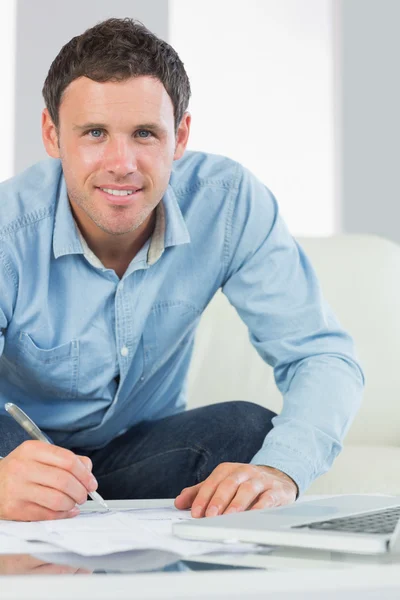 Happy casual man writing on sheets paying bills — Stock fotografie