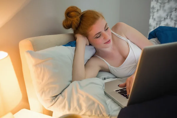 Bella rossa sdraiata sul suo letto con il computer portatile — Foto Stock