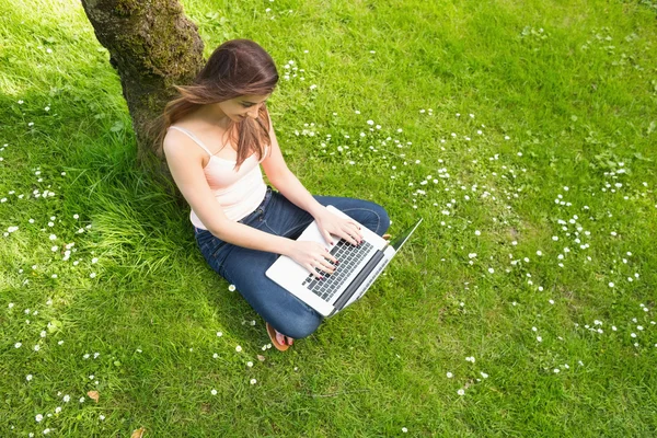 Leuke vrouw leunend tegen een boom met behulp van haar notitieblok — Stockfoto