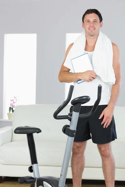 Glada sportiga man står bakom motionscykel håller tablet — Stockfoto