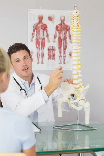 Atractivo médico mostrando a un paciente algo en el modelo de esqueleto — Foto de Stock