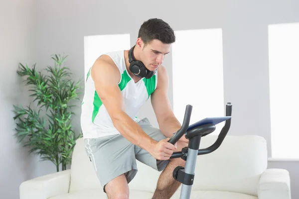 Deportivo hombre guapo entrenamiento en bicicleta estática usando tableta — Foto de Stock