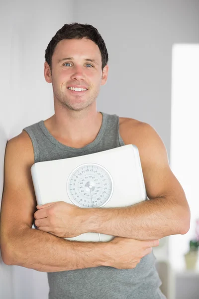 Sporty smiling man leaning against wall holding a scale — Stock Photo, Image