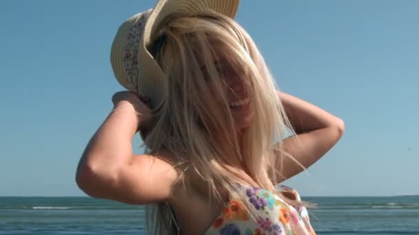 Attractive blonde turning with straw hat on beach — Stock Video