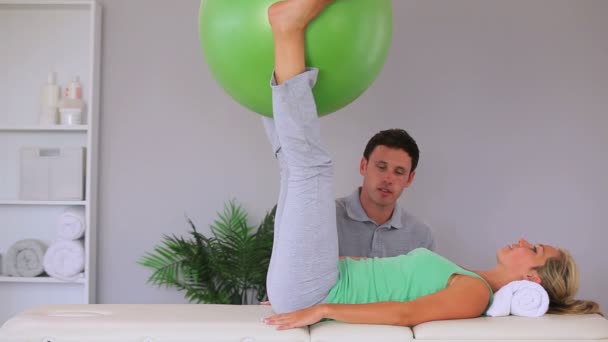 Fyzioterapeut, sledovat jeho pohyb pacienta cvičení míč mezi její kolena — Stock video