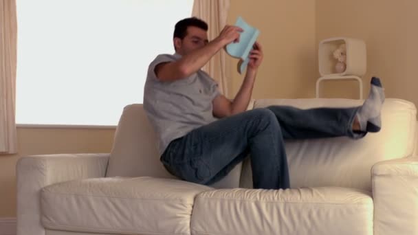 Homem atraente pulando no sofá com livro — Vídeo de Stock