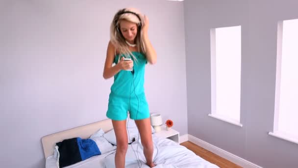 Attraktive Blondine tanzt auf dem Bett und hört Musik — Stockvideo