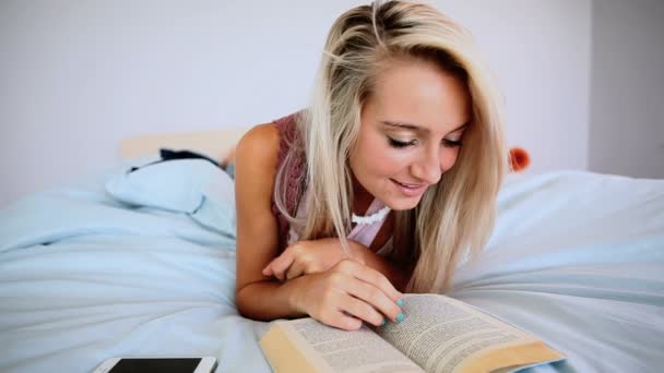 Atractiva rubia acostada en la cama leyendo libro — Vídeos de Stock