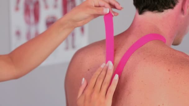 Fisioterapeuta aplicando cinta de cinesio rosa a pacientes varones espalda — Vídeo de stock
