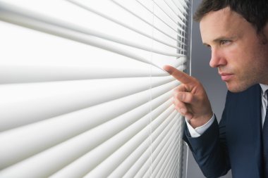 Stern attractive businessman spying through roller blind clipart