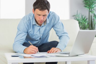 Serious casual man writing on sheets paying bills clipart