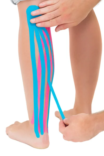 Physiotherapist applying pink and blue kinesio tape on patients leg — Stock Photo, Image