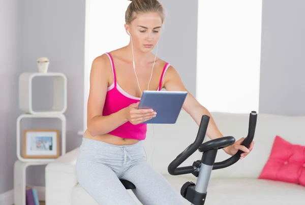 Entrenamiento rubio deportivo enfocado en bicicleta estática usando tableta —  Fotos de Stock