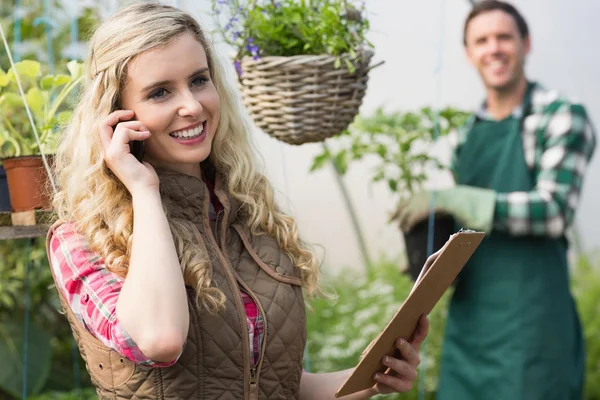 Smiling blonde woman phoning in a green house — Stock Photo, Image