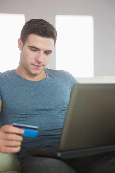 Conteúdo homem bonito relaxando no sofá usando laptop compras on-line — Fotografia de Stock