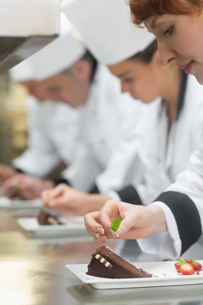 Team of young chefs in a row garnishing dessert plates — Stock Photo, Image