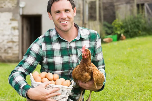 Happy young man holding his chicken and basket of eggs — Stock Photo, Image