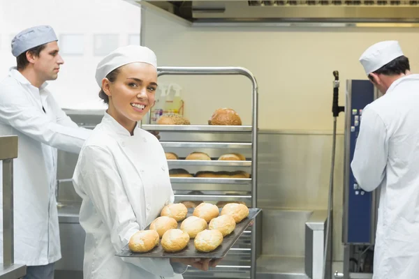 Niedliche junge Bäckerin hält ein Backblech mit Brötchen drauf — Stockfoto