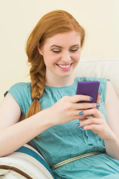 Glad rödhårig sitter i soffan med smartphone — Stockfoto