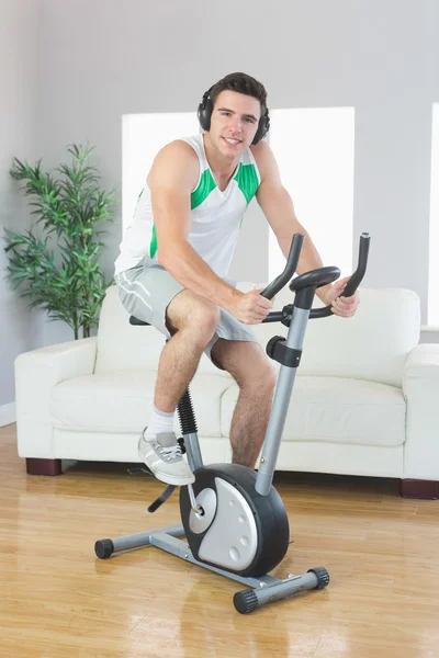 Hombre guapo alegre entrenando en bicicleta estática escuchando música — Foto de Stock