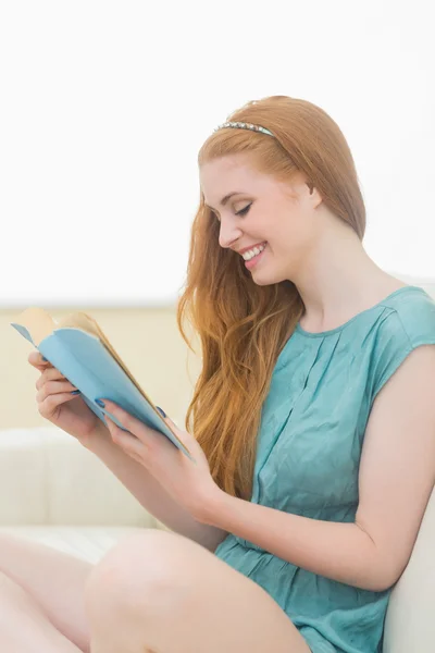 Feliz pelirroja leyendo un libro en el sofá — Foto de Stock