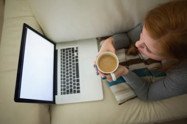 Rossa sdraiata sul divano a guardare il computer portatile che prende un caffè — Foto Stock